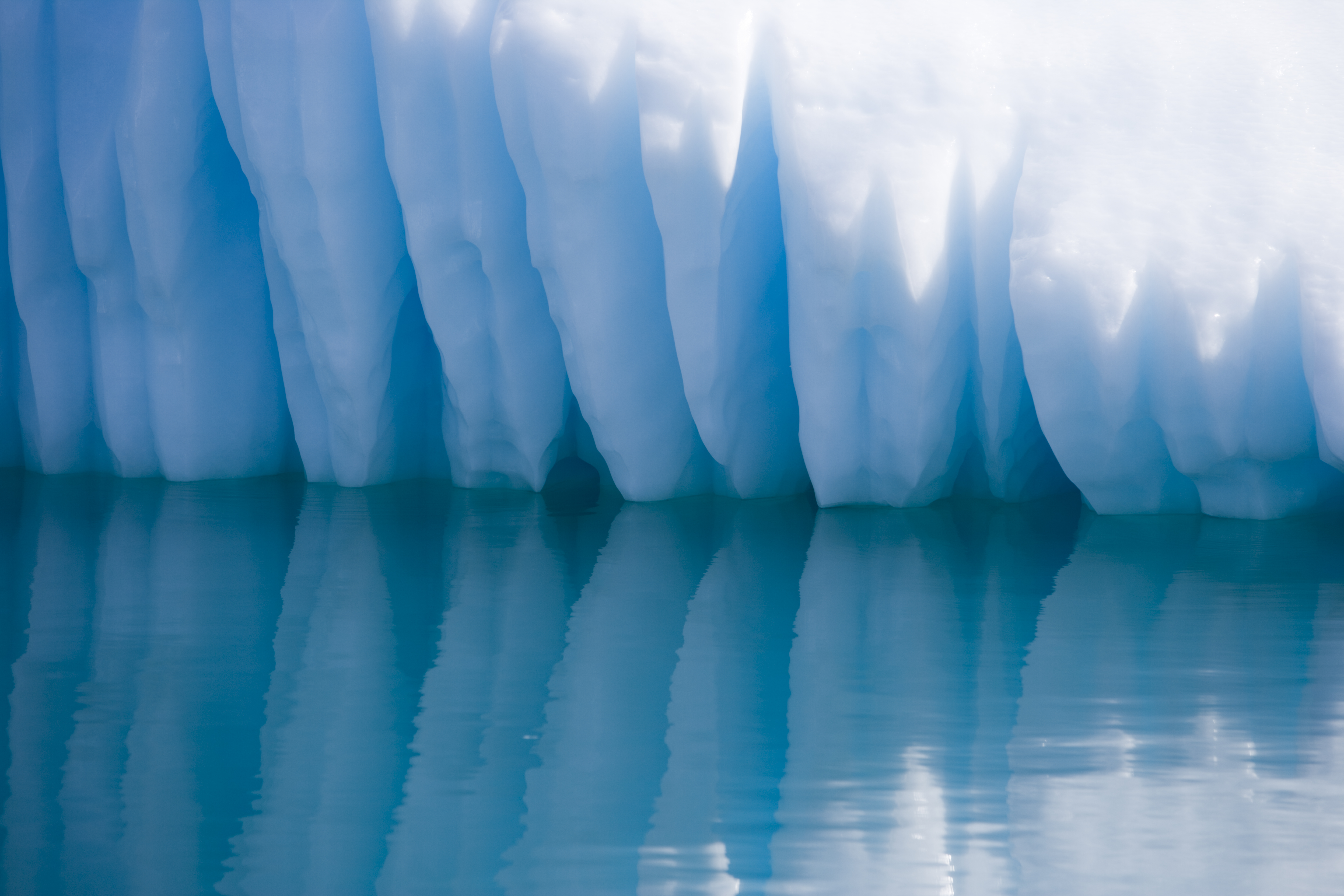 Qooroq Fjord, Grönland: Ein Eisberg, der wie eine Reihe scharfer, gigantischer Zähne aus dem Meer ragt. Die zerklüfteten Spitzen und tiefen Rillen des Eises erinnern an ein gewaltiges Gebiss, das aus der Tiefe des Ozeans emporsteigt. Die schimmernden Blautöne des Eises verstärken den surrealen Eindruck, während die Sonnenstrahlen die Kanten betonen und Schatten werfen, die die bedrohliche Ästhetik des Naturphänomens unterstreichen. Foto: © Holger Leue / leue-photo.com