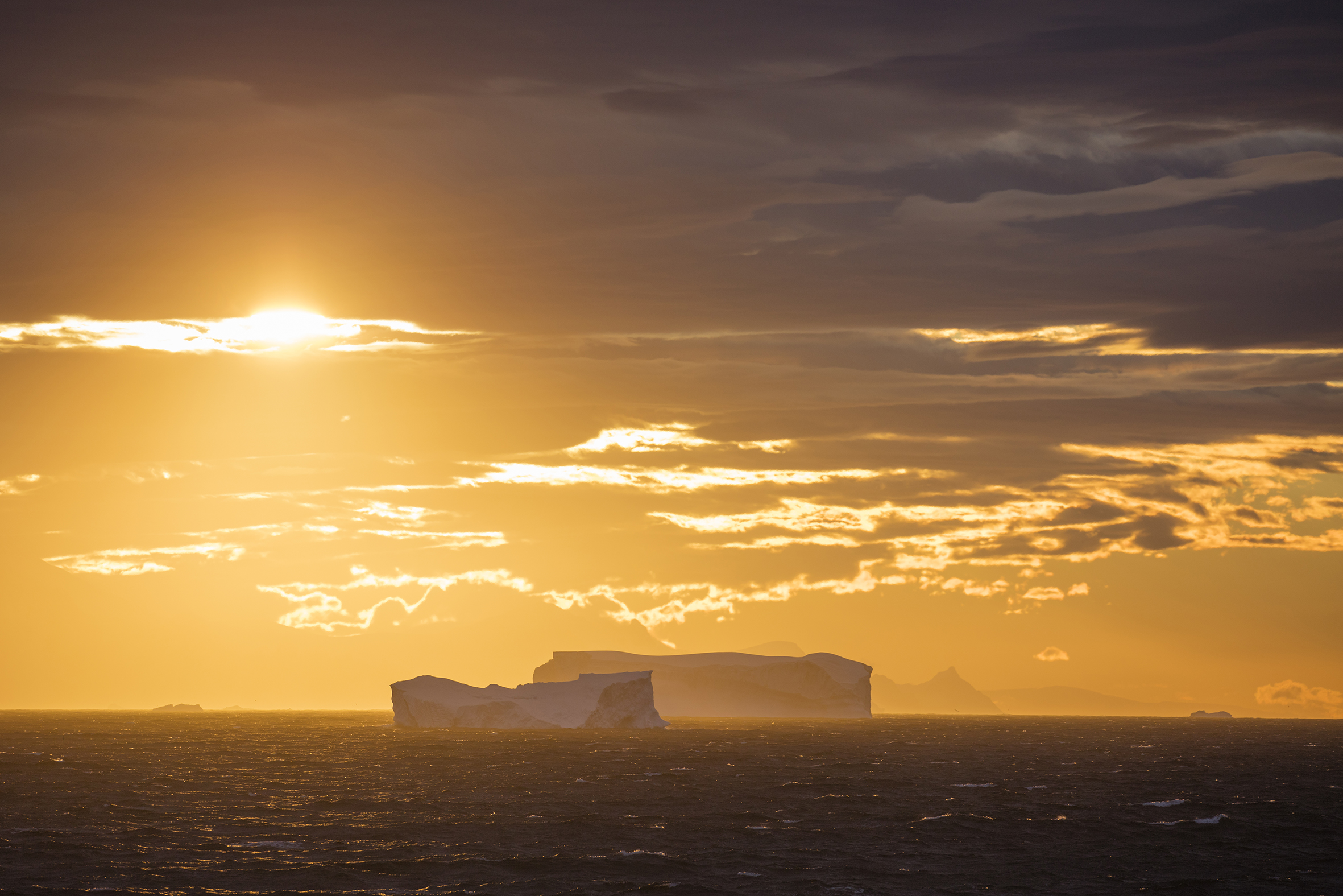 Bei Sonnenuntergang verwandelt sich die Antarktis in ein magisches Panorama, in dem die Silhouetten schwimmender Eisberge vor einem leuchtend goldenen Himmel erscheinen. Die klare, kalte Luft verstärkt die Farbenpracht und die scharfen Konturen der Eises. Foto: © Holger Leue / leue-photo.com