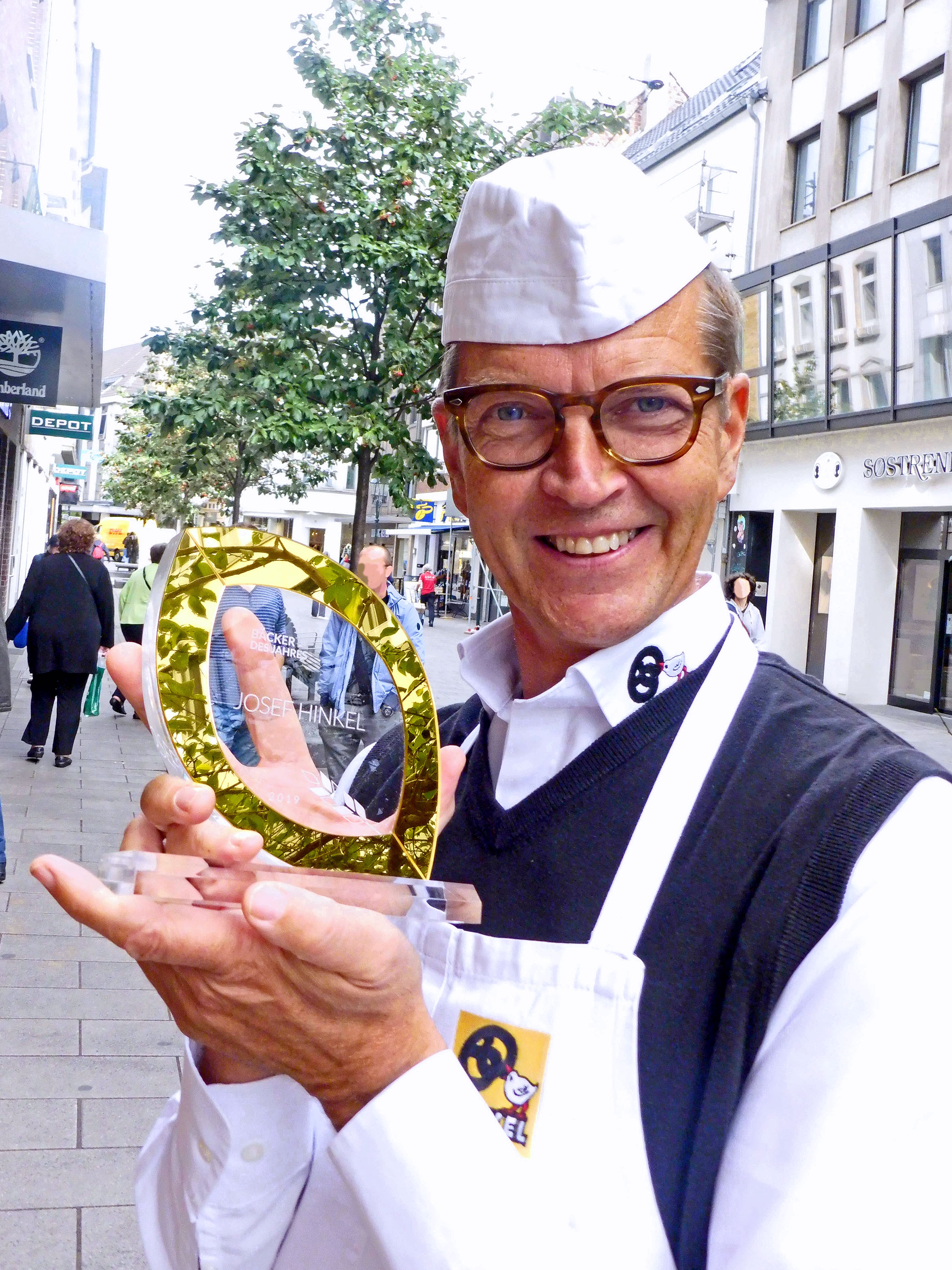 Josef Hinkel präsentiert stolz den Preis vor seiner Bäckerei am Carlsplatz in Düsseldorf. Foto: © Privat