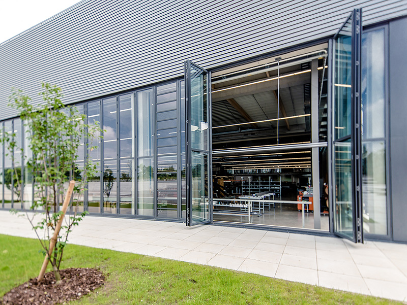 Glas-Faltwände in den Produktionshallen lassen sich komplett zur Seite öffnen und verbinden den Arbeitsbereich mit der anliegenden Natur. Foto: © Solarlux GmbH