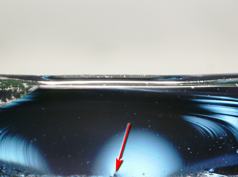 An der Unterkante des Bruchspiegels ist der Beginn des Drucksprungs an der Unregelmäßigkeit erkennbar (Pfeil), Hier trat die größte Zugspannung auf. Foto: © Ekkehard Wagner