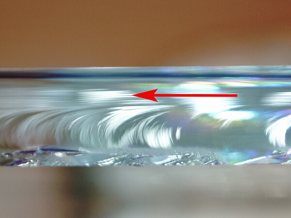 Wallner-Linien zeigen die Bruchlaufrichtung (Pfeil) an und die Oberfläche mit Druckspannung (oben) und mit Zugspannung (unten). Foto: © Ekkehard Wagner
